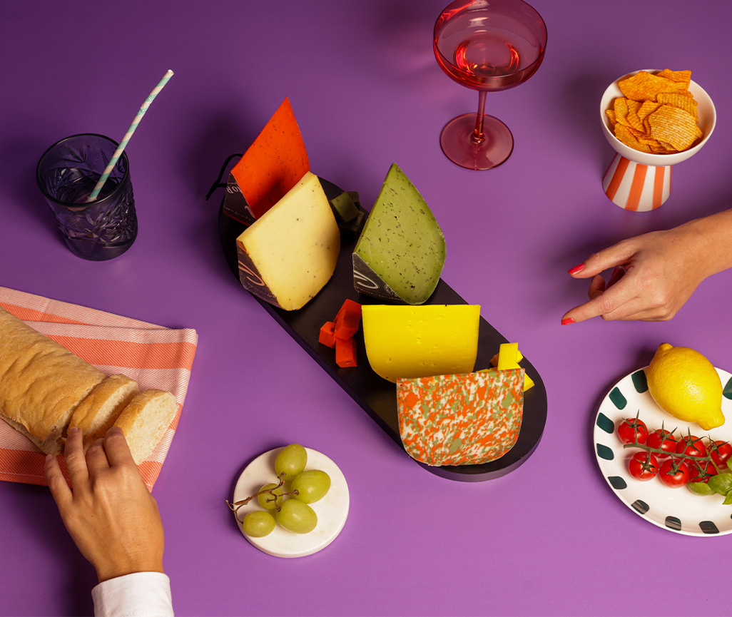 Tafel vol kaas met brood, cocktail glas en groente en fruit. Vrouw aan het lunchen